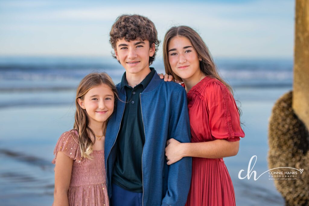 Family photos at Scripps Pier, La Jolla Beach. Stylized family with toes in sand at pier and cliffs.