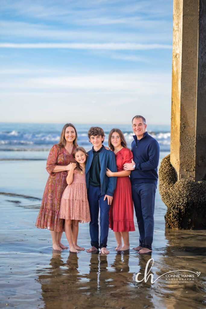 Family photos at Scripps Pier, La Jolla Beach. Stylized family with toes in sand at pier and cliffs.