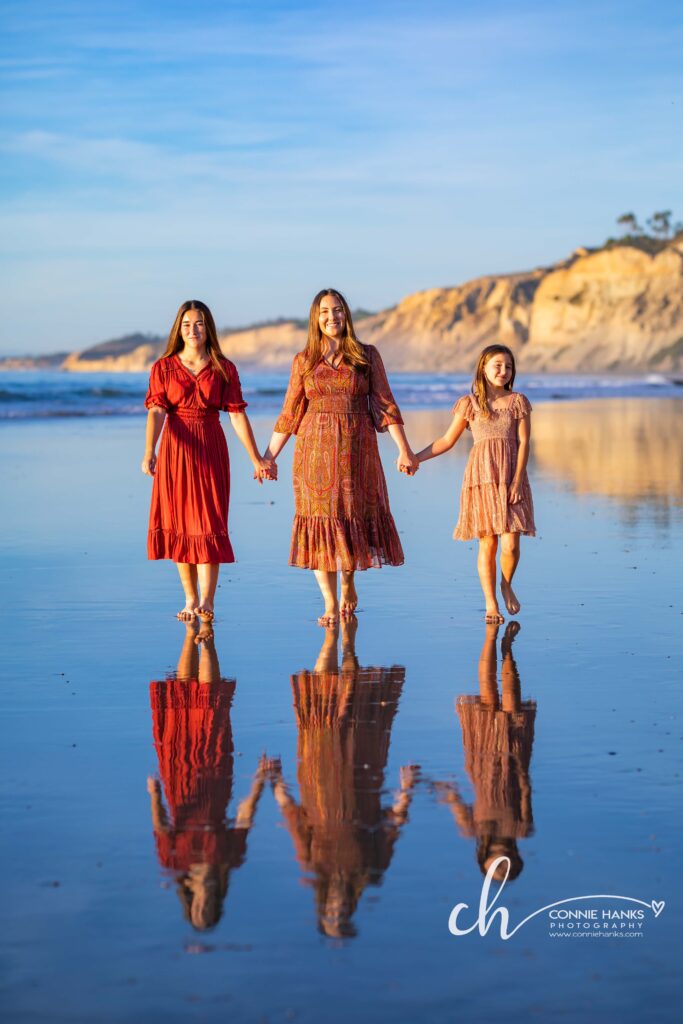 Family photos at Scripps Pier, La Jolla Beach. Stylized family with toes in sand at pier and cliffs.