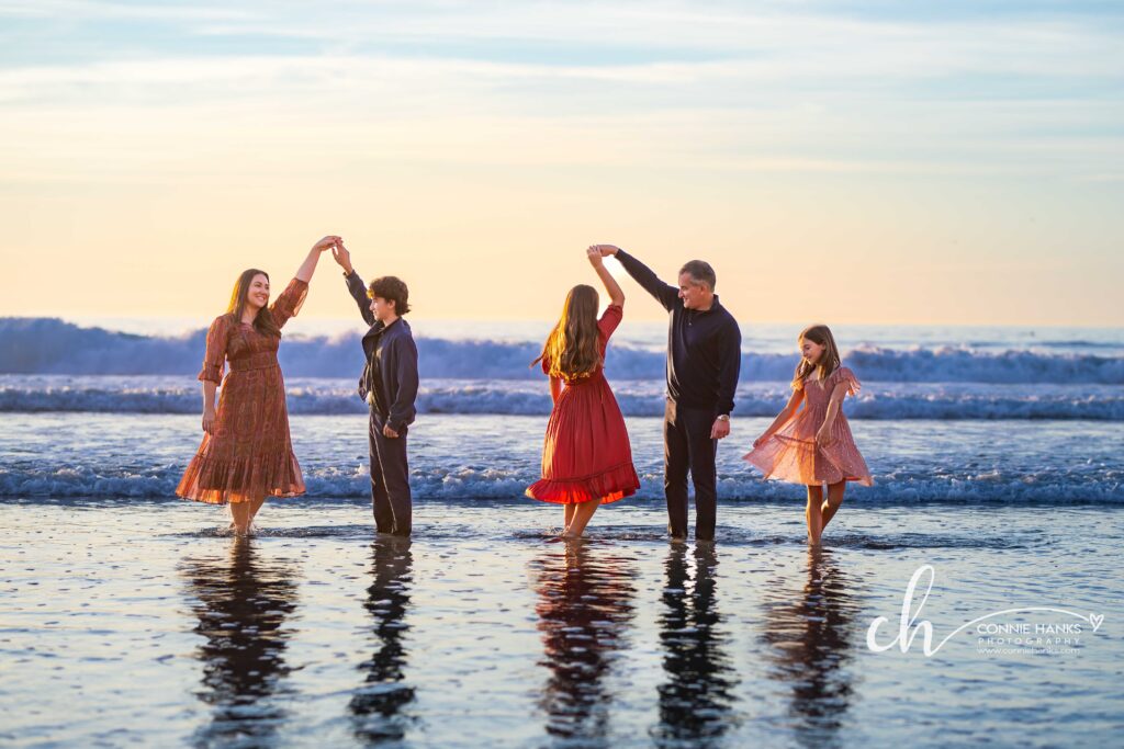 Family photos at Scripps Pier, La Jolla Beach. Stylized family with toes in sand at pier and cliffs.
