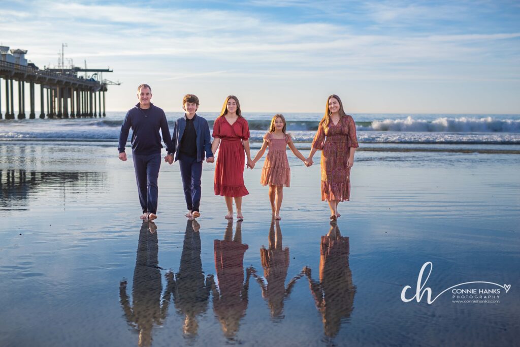 Family photos at Scripps Pier, La Jolla Beach. Stylized family with toes in sand at pier and cliffs.