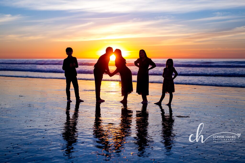 Family photos at Scripps Pier, La Jolla Beach. Stylized family with toes in sand at pier and cliffs.
