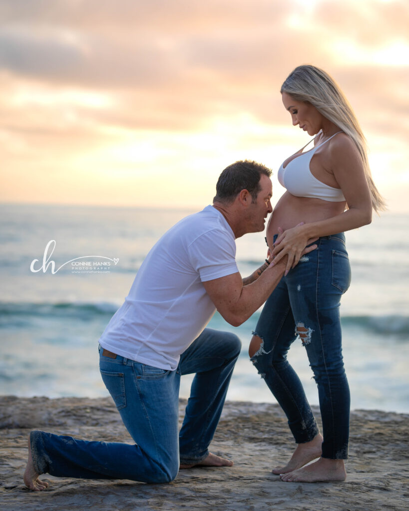 Maternity photos at Windansea Beach, La Jolla. Couple on cliffs along beach with painterly sunset skies.