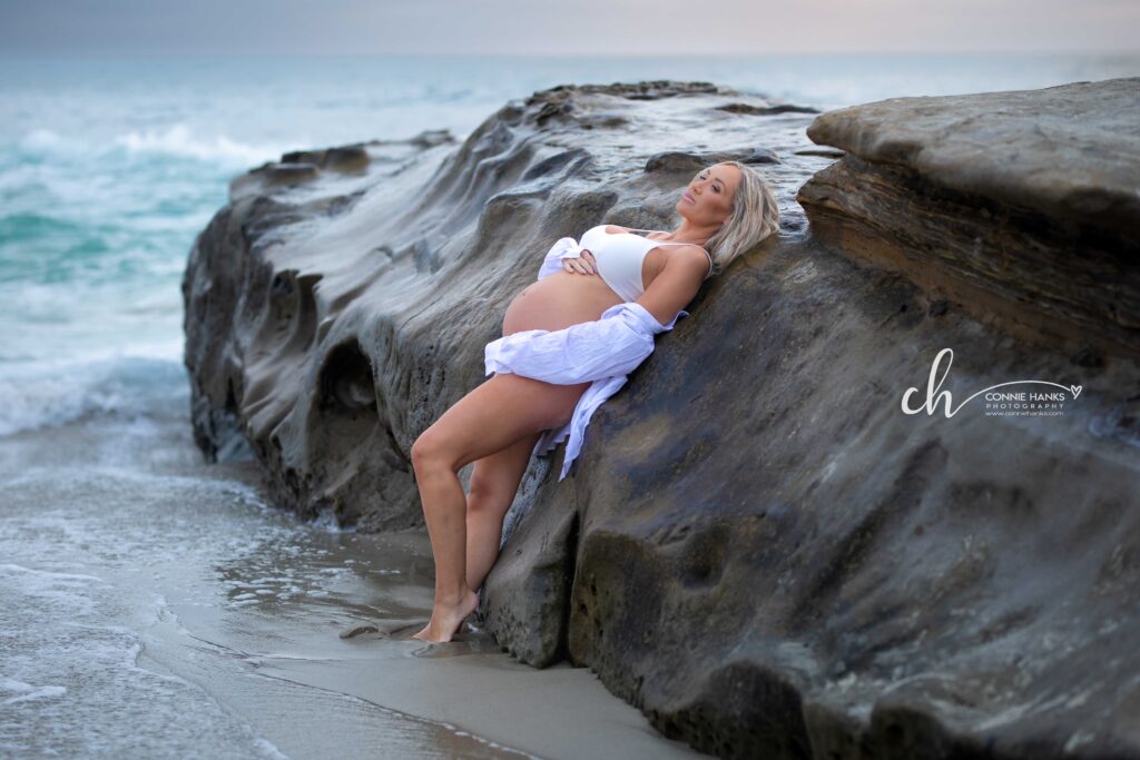 Maternity photos at Windansea Beach, La Jolla. Pregnant woman leaning on rocks at beach.