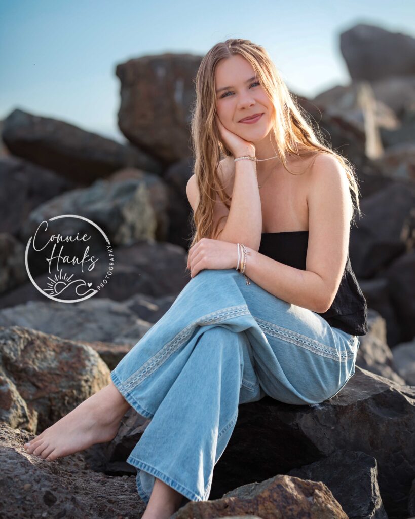 Senior photos at Coronado. Girl sitting on rock formation at beach.