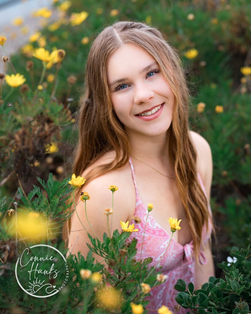 Senior photos at Coronado. Girl surrounded by lush plants and yellow flowers.